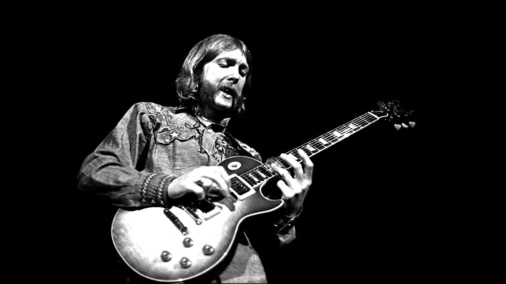 Eric Clapton passionately plays electric guitar in all denim on dark stage background wallpaper