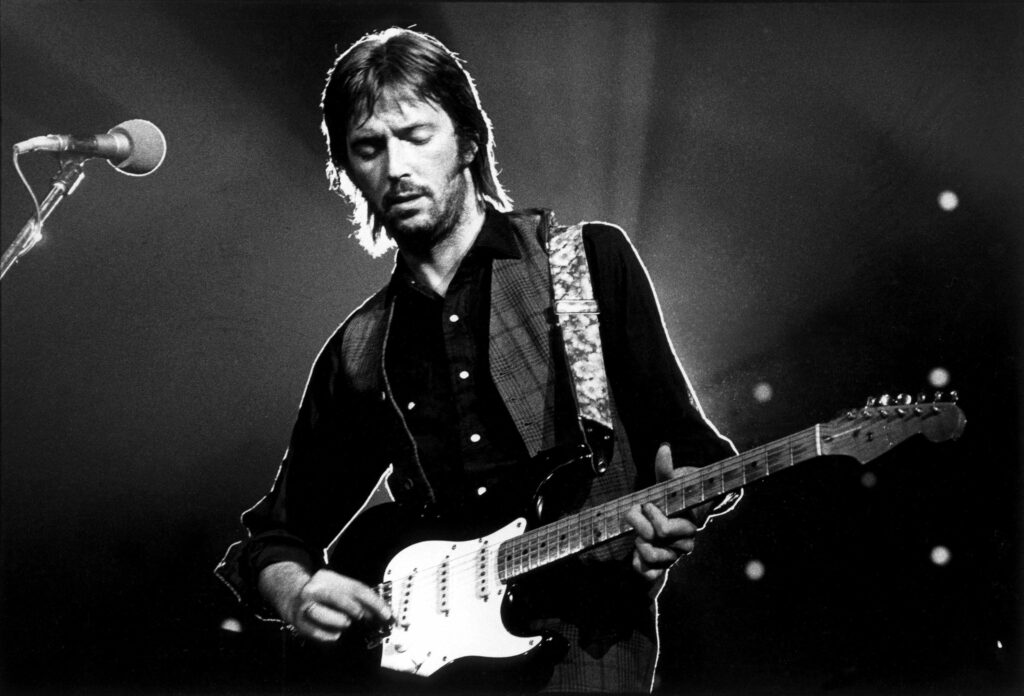 Eric Clapton playing electric guitar under spotlight on stage creating iconic music scene wallpaper