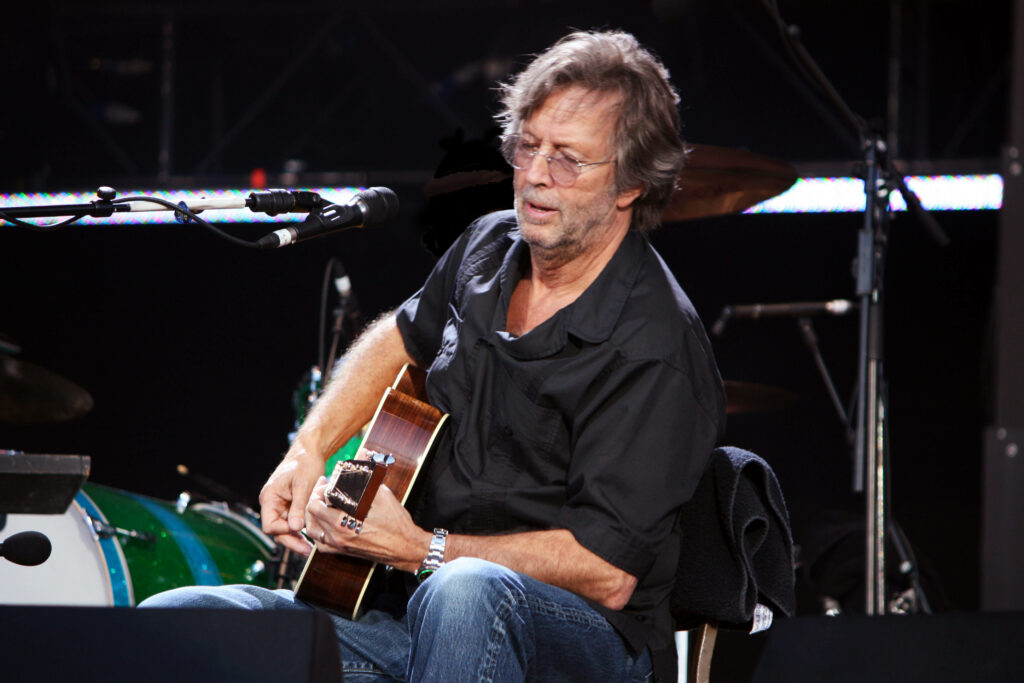 Eric Clapton playing guitar live on stage wearing black polo shirt immersive performance wallpaper