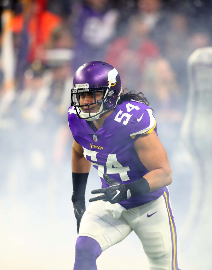 Eric Kendricks in Minnesota Vikings uniform charging on field with vibrant stadium lights and smoke Wallpaper