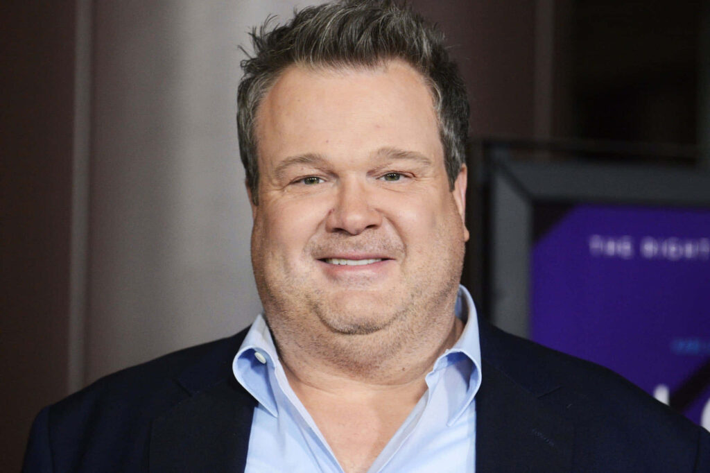 Close-up of Eric Stonestreet in dark suit and blue shirt with soft muted background wallpaper