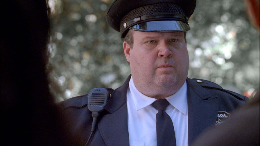 Eric Stonestreet in police uniform serious pose natural daylight blurred greenery background wallpaper
