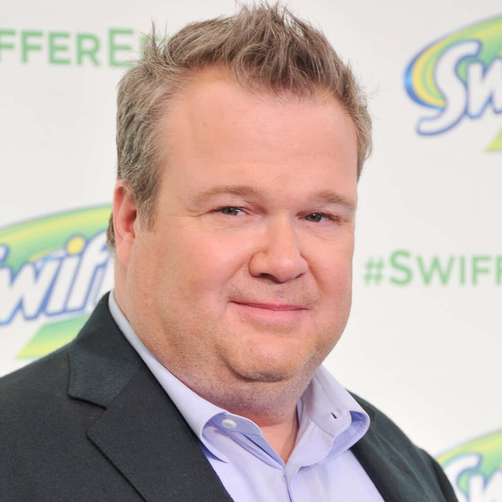 Eric Stonestreet in sharp suit confident pose bright lighting branded backdrop vibrant wallpaper