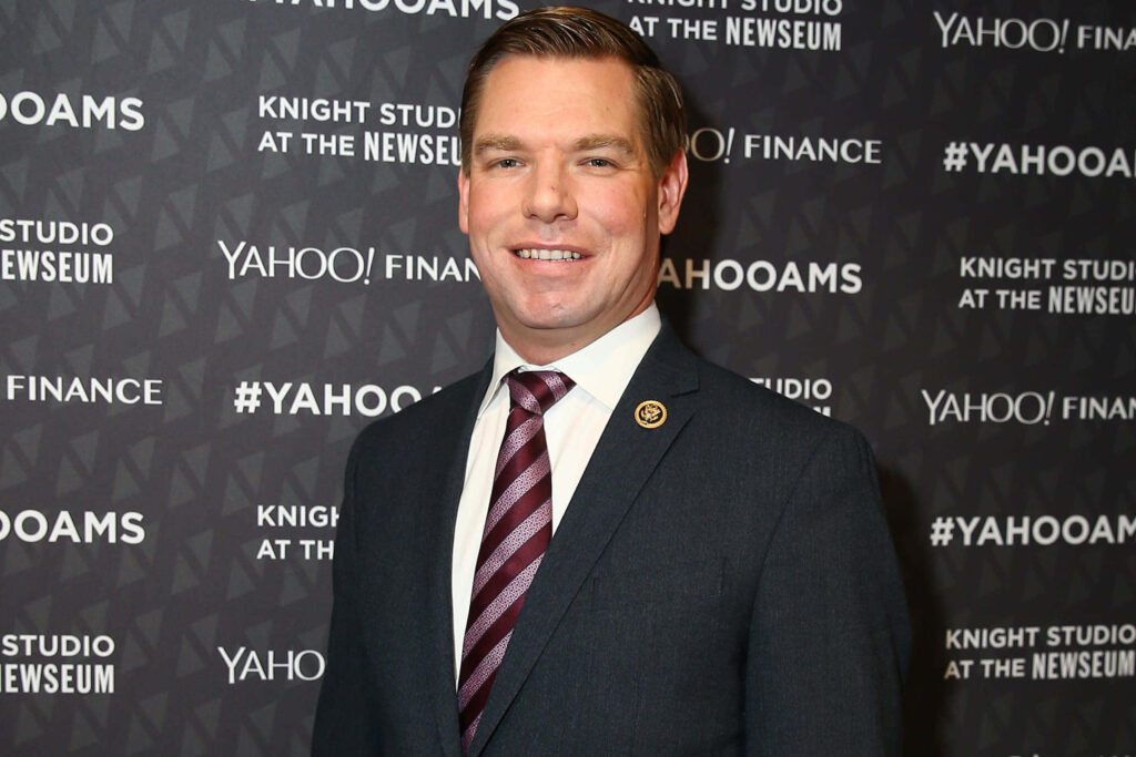 Eric Swalwell in formal suit and striped tie at Yahoo Finance event with professional warm lighting Wallpaper