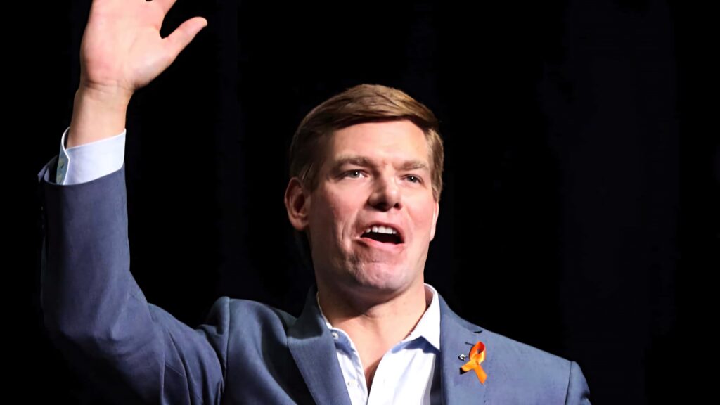 Eric Swalwell confident politician with raised hand dark background orange ribbon lapel pin wallpaper