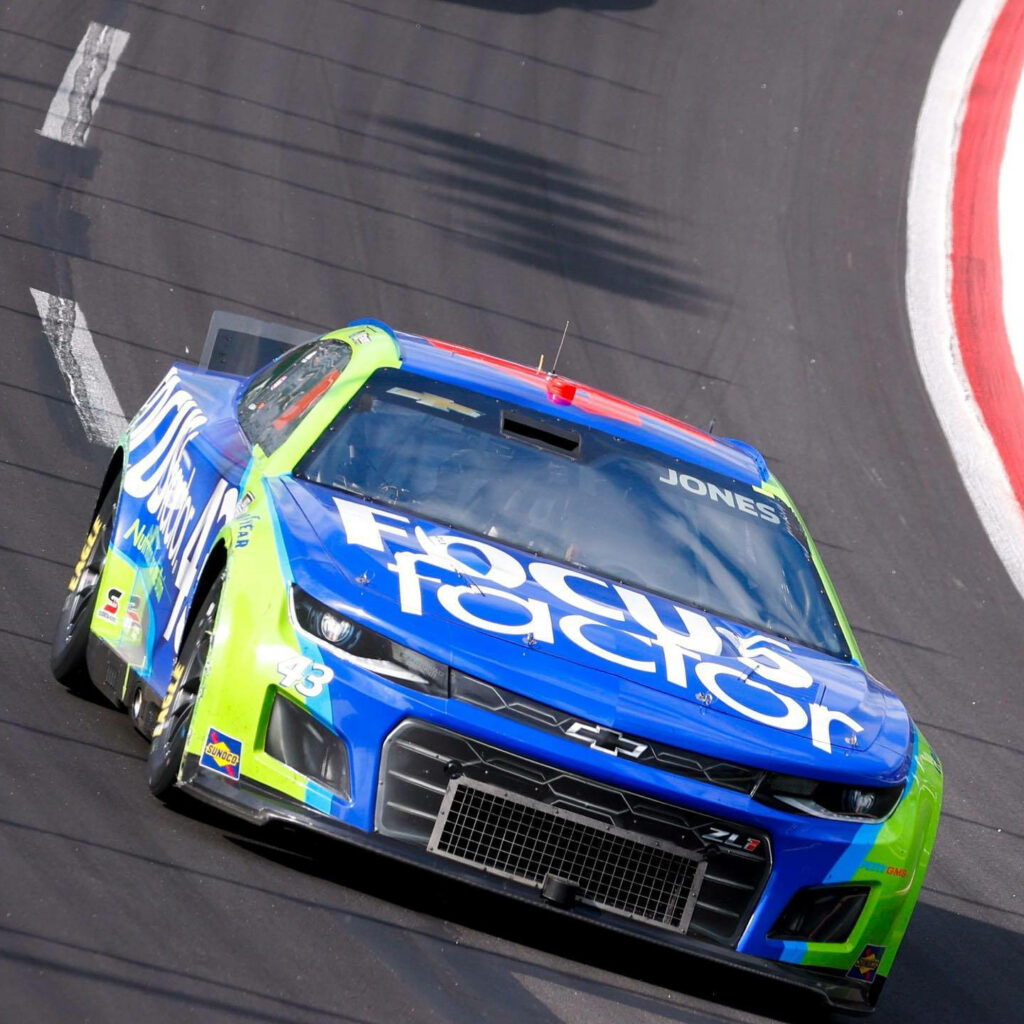 Erik Jones racing car with Focus Factor branding in blue and green speeds on racetrack wallpaper