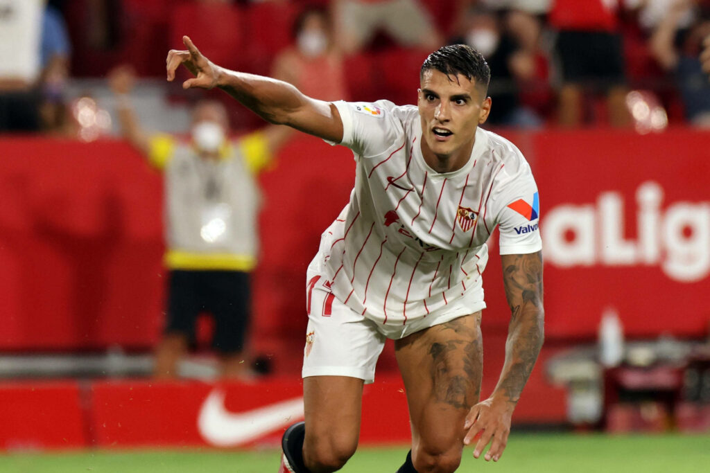 Érik Lamela in Sevilla FC white and red kit mid-action on football field vibrant stadium scene Wallpaper