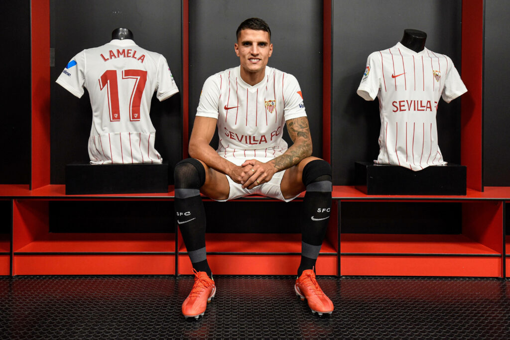 Érik Lamela in Sevilla FC white kit with red pinstripes sitting in locker room with jerseys Wallpaper