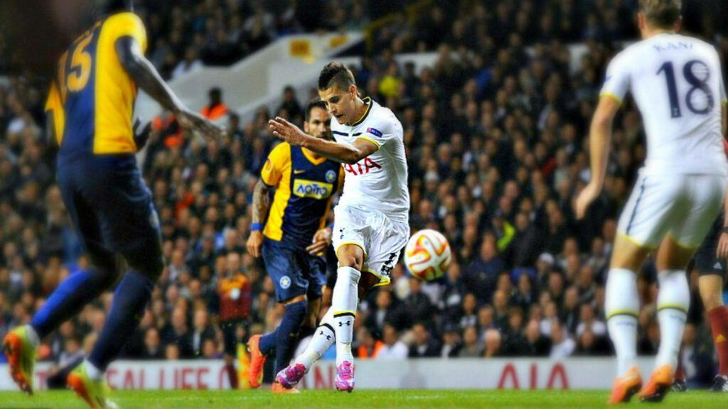 Erik Lamela in Tottenham kit striking ball on vibrant pitch with packed stadium background Wallpaper