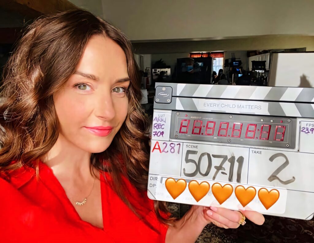 Erin Karpluk smiling with Every Child Matters clapperboard in warm film set lighting red top Wallpaper