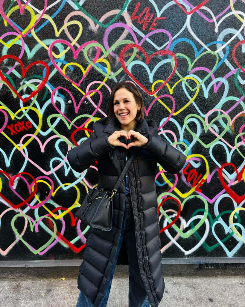 Erin Krakow smiling making heart shape hands in black coat vibrant graffiti hearts and love words background Wallpaper
