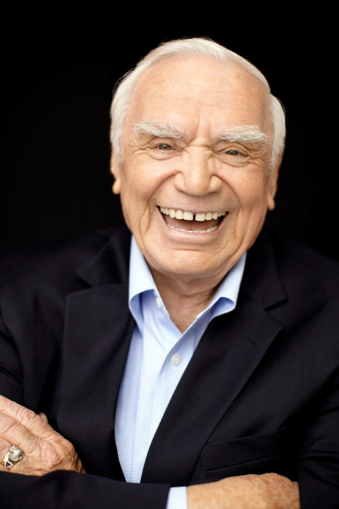 Ernest Borgnine portrait in dark suit and blue shirt smiling warmly on black background wallpaper