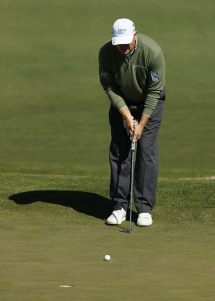 Ernie Els focused on putting golf ball on lush green course in classic golf attire wallpaper
