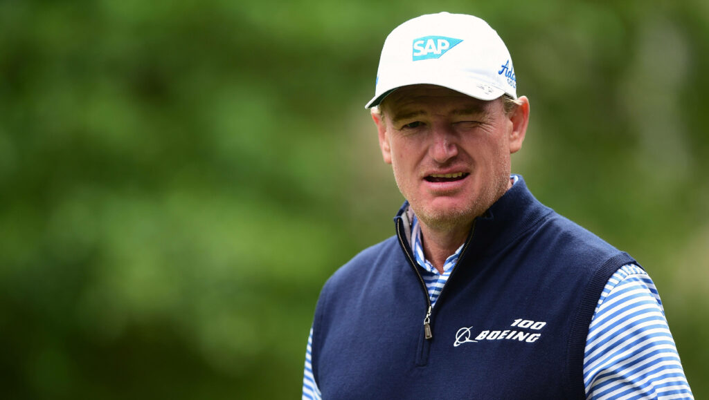 Close-up of golfer Ernie Els in navy vest and white cap with blurred green golf course background Wallpaper
