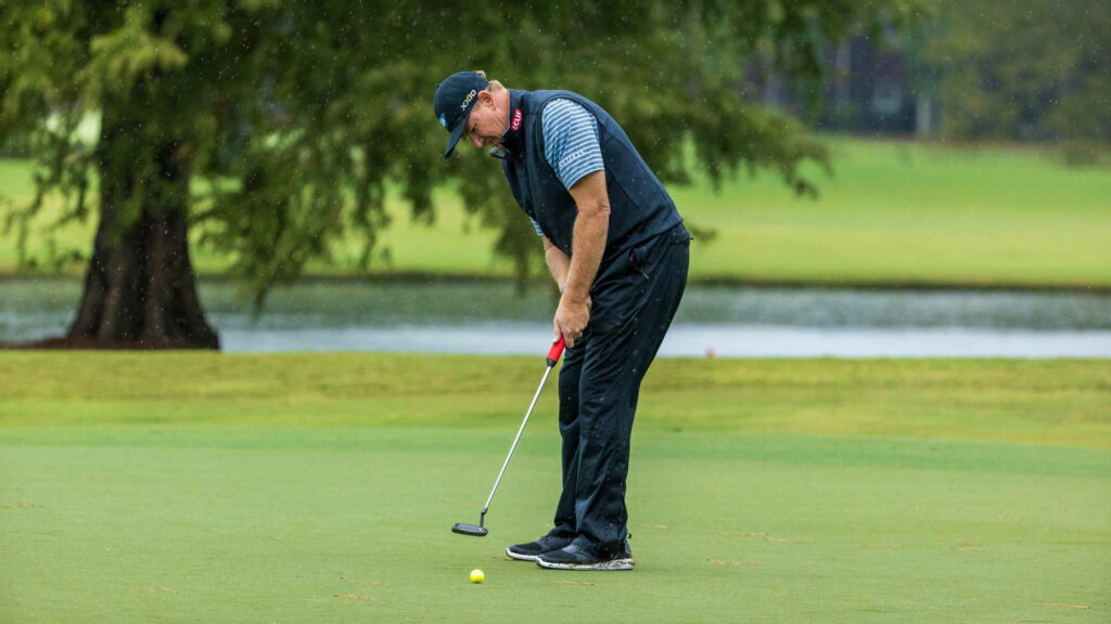 Ernie Els focused on putting on lush green golf course with serene natural background wallpaper