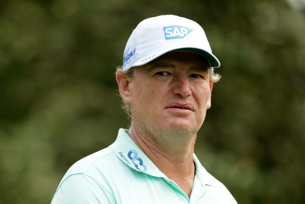 Ernie Els focused in light polo and white SAP cap against soft green golf background wallpaper