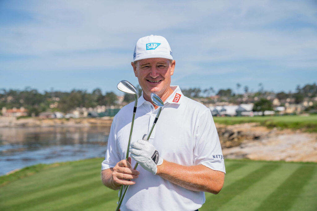 Ernie Els smiling on golf course with signature clubs waterfront backdrop professional attire Wallpaper