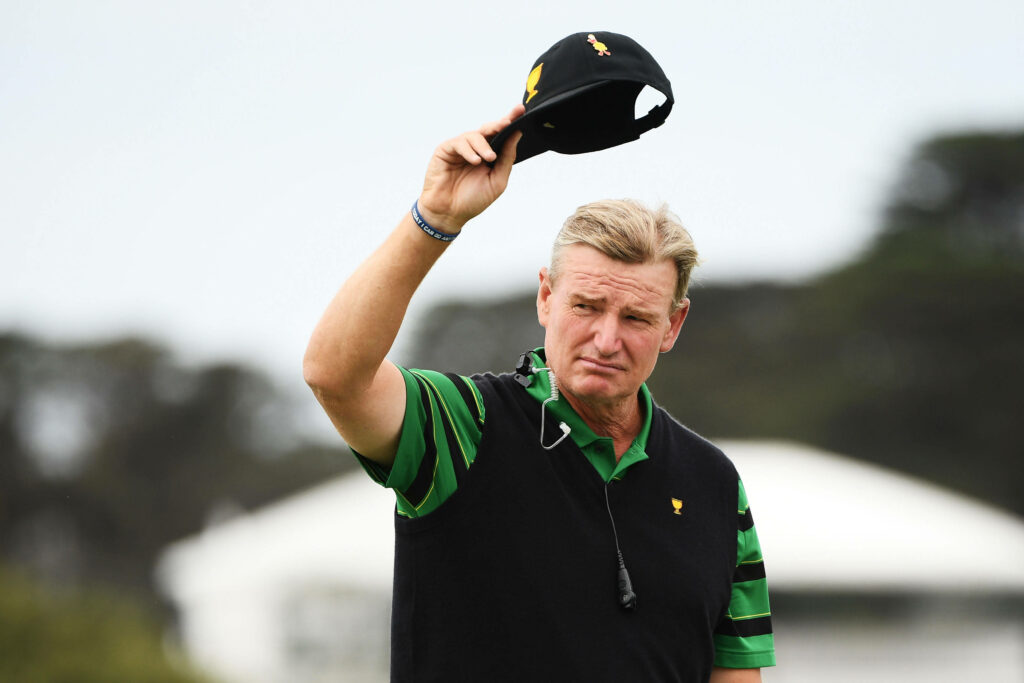 Golf legend Ernie Els salutes fans raising his cap with composed expression on clear sky background Wallpaper