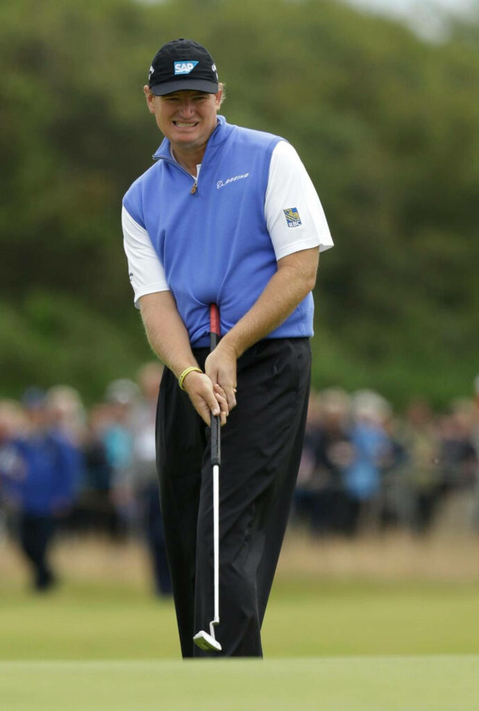 Ernie Els focused mid-putt on lush green golf course wearing blue vest and black cap tournament play Wallpaper
