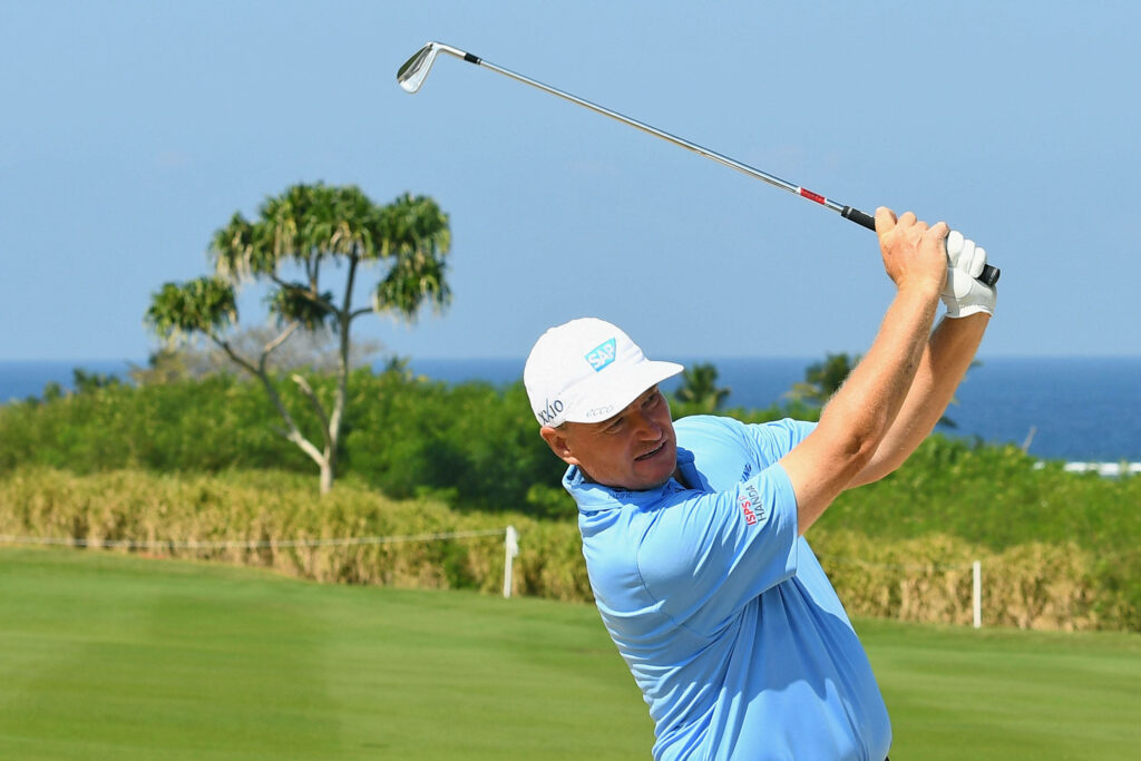 Ernie Els mid swing on lush golf course with green fairways blue skies tropical ocean backdrop Wallpaper
