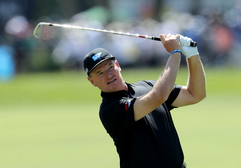 Ernie Els mid golf swing on sunny course wearing black shirt and cap showing focused precision Wallpaper