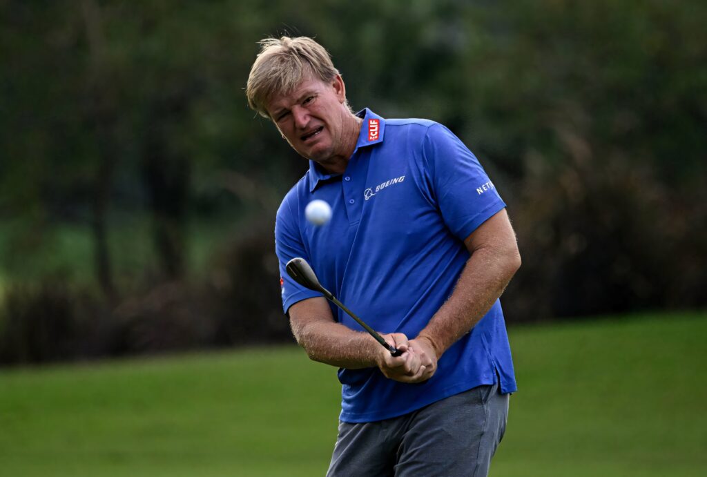 Ernie Els mid-swing chipping golf ball on vibrant green course in blue polo shirt professional golf Wallpaper
