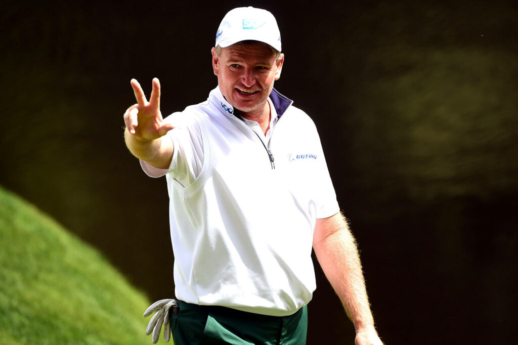 Ernie Els on golf course making peace sign wearing athletic attire with green and gold background Wallpaper