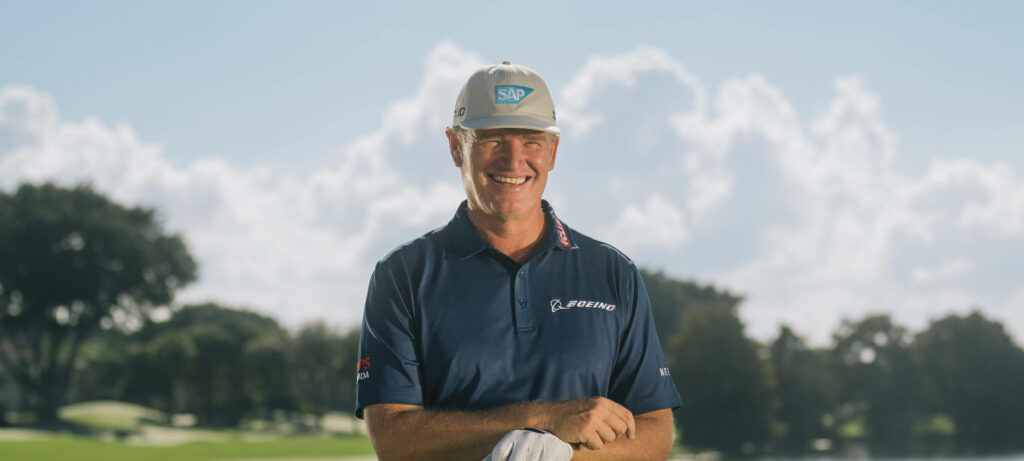 Ernie Els smiling on sunny golf course wearing blue polo white cap with green trees background Wallpaper