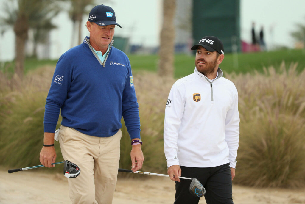 Ernie Els and Louis Oosthuizen walking on golf course with clubs palm trees and sand background Wallpaper