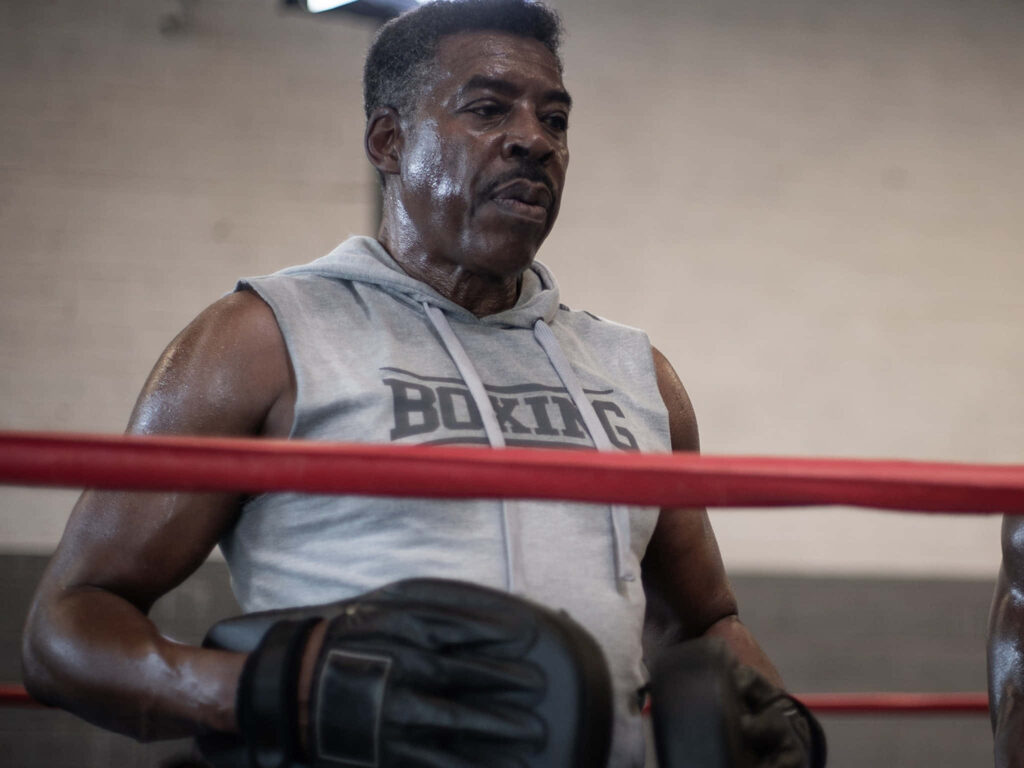 Ernie Hudson in gray Boxing hoodie and gloves in ring showing strength and determination training Wallpaper