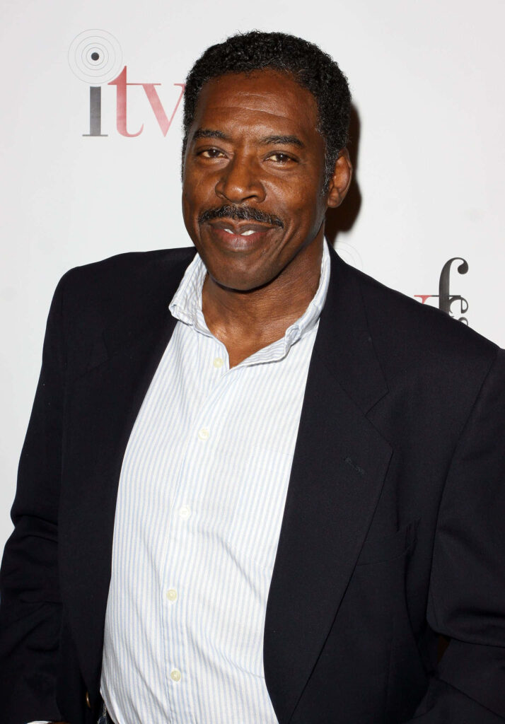 Ernie Hudson portrait in dark blazer smiling against white backdrop with subtle ITV logo wallpaper