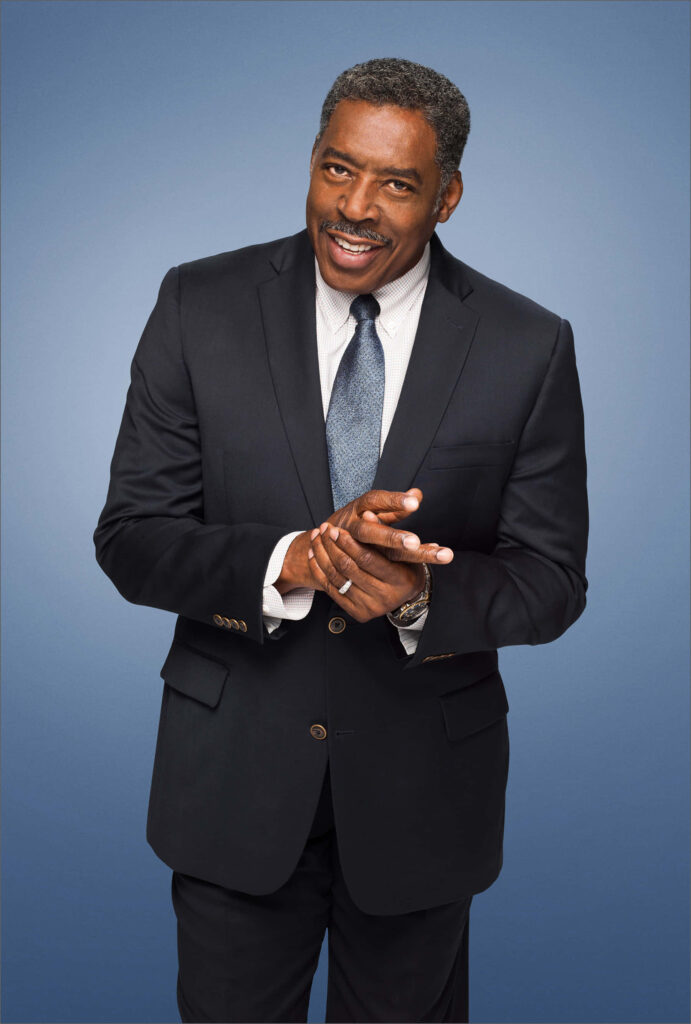 Ernie Hudson confident portrait in dark suit white shirt patterned tie blue gradient background Wallpaper