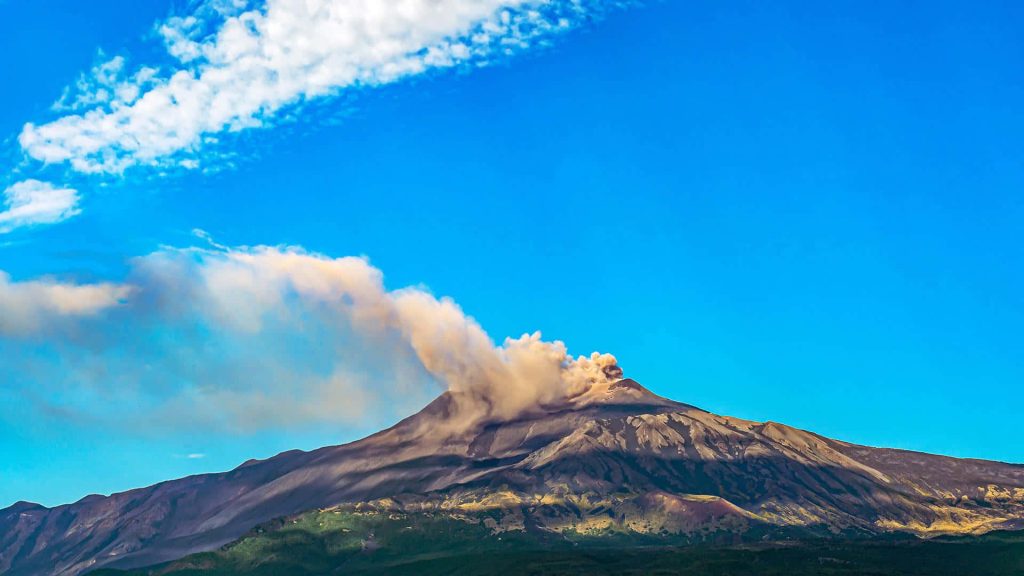 Erupting Mount Etna with smoke plume over rugged Sicilian landscape and bright blue sky wallpaper