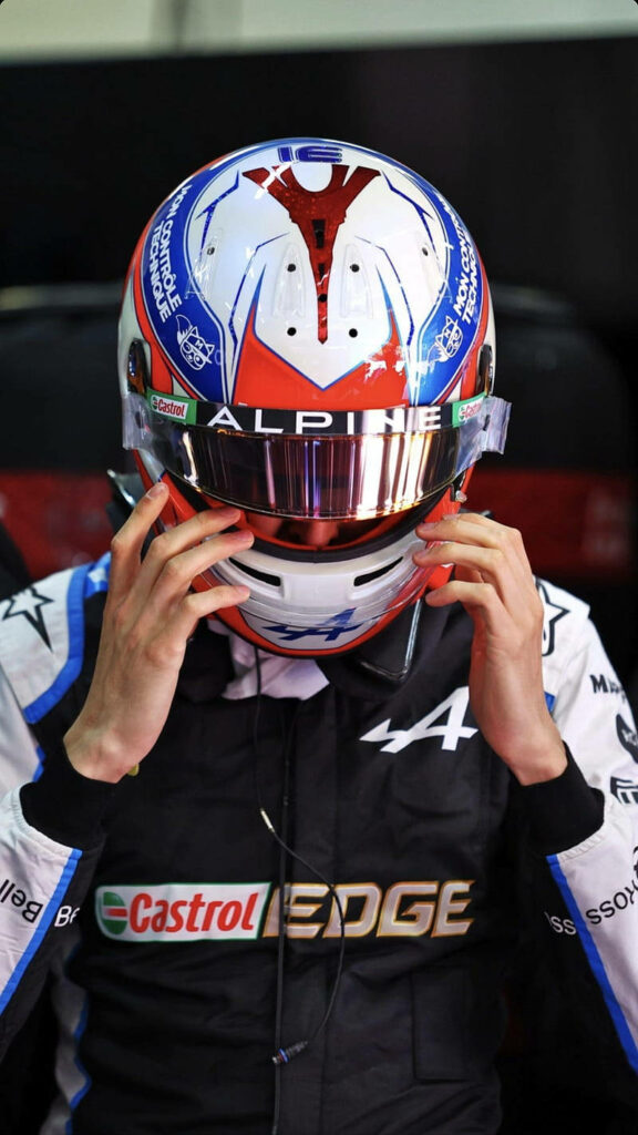 Esteban Ocon in Alpine F1 suit and helmet with blue white red accents racing wallpaper background