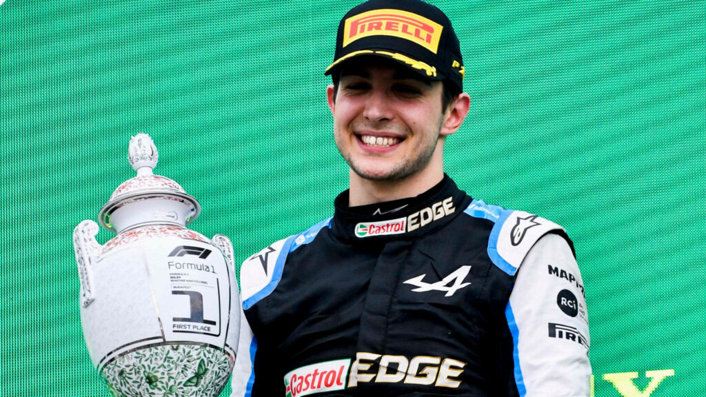 Esteban Ocon celebrating on Formula 1 podium holding trophy in Alpine suit vibrant green background Wallpaper