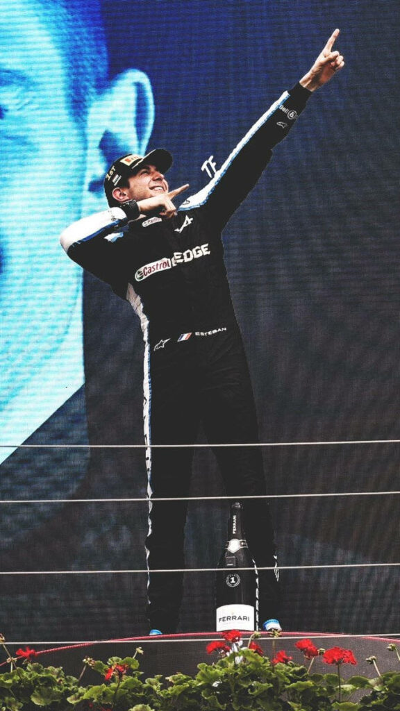 Esteban Ocon celebrates Formula 1 victory on podium in racing suit with dynamic energetic pose Wallpaper