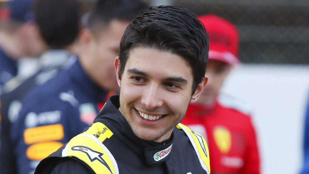 Esteban Ocon smiling in racing suit with vibrant Formula 1 paddock background wallpaper