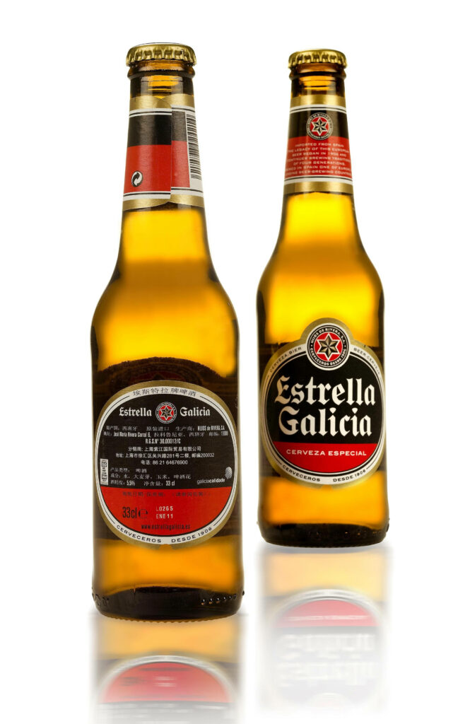 Two Estrella Galicia beer bottles with golden amber color and crisp reflections on white background Wallpaper