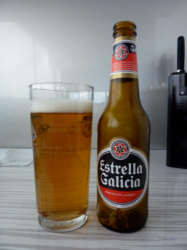 Estrella Galicia Premium Lager bottle and glass of golden beer on light striped surface wallpaper
