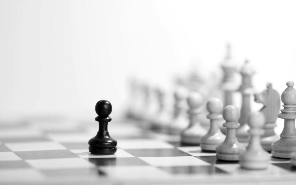 Contrasting Clash: A Bold Black Pawn Confronting Fading White Chess Pieces on a Minimalistic Background Wallpaper