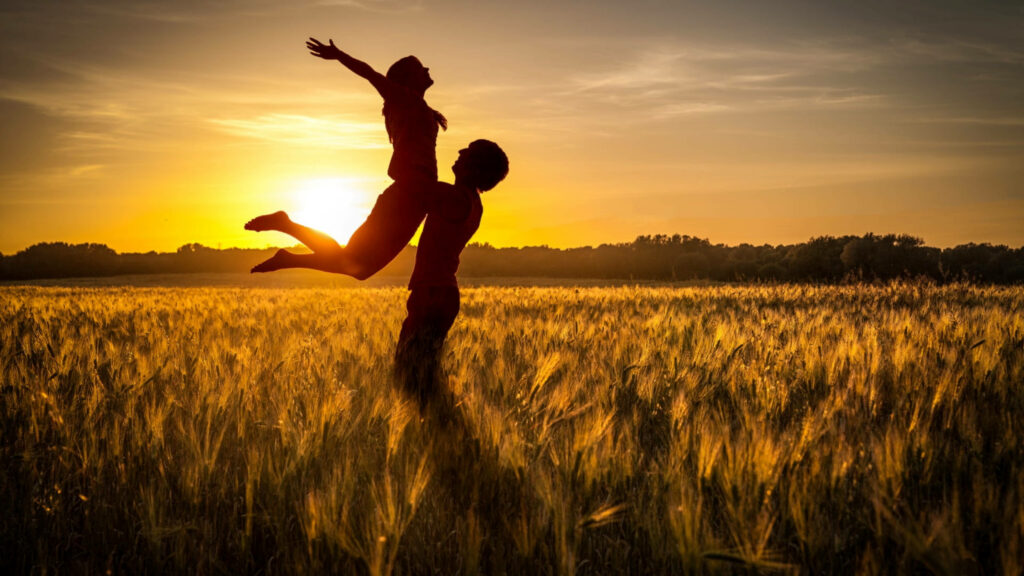 Romantic Sunset Serenade: Enchanting Silhouette of Dancing Lovers Amidst a Field Wallpaper