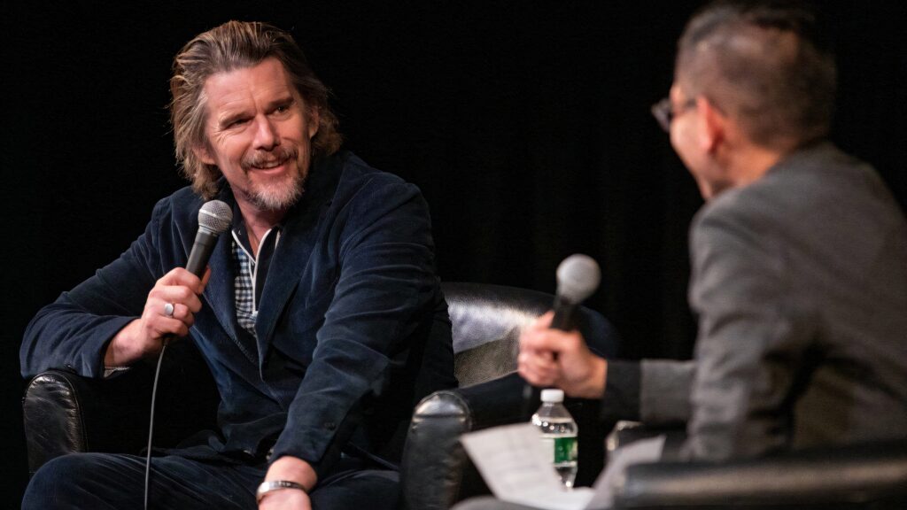 Ethan Hawke smiling warmly during candid interview with relaxed pose and cozy lighting background Wallpaper