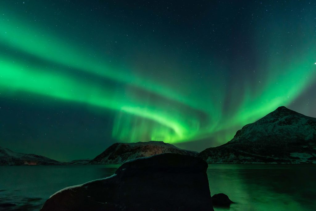 Aurora Borealis glowing green over snow-capped mountains reflected in calm arctic waters at night Wallpaper
