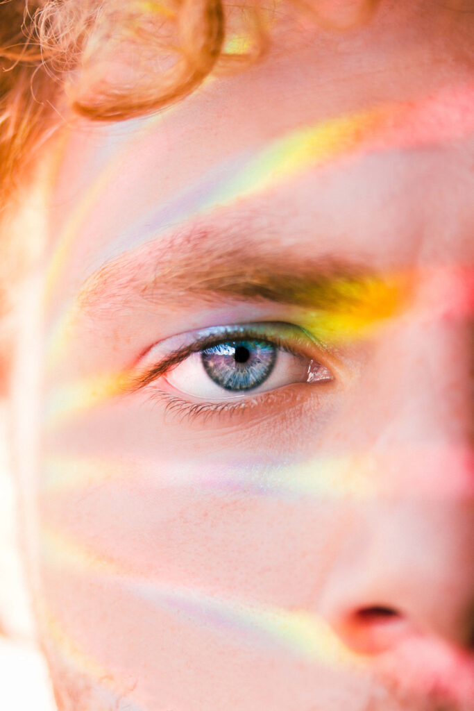 Closeup of blue eye with rainbow light rays on warm skin for dreamy modern artistic portrait wallpaper