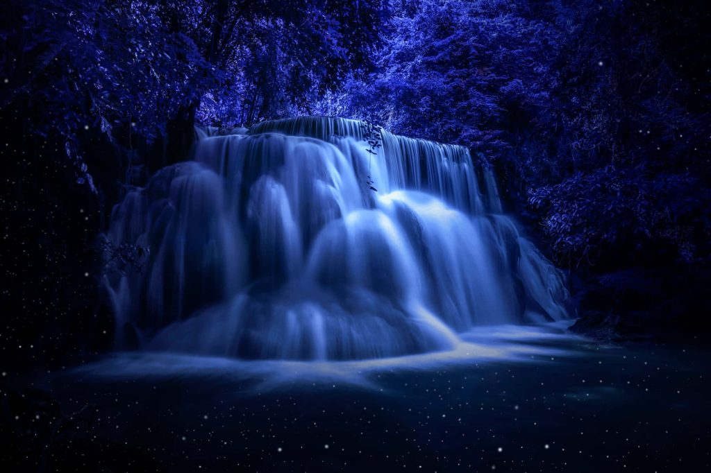 Ethereal deep blue waterfall long exposure with glowing cascade in mystical dense forest background Wallpaper