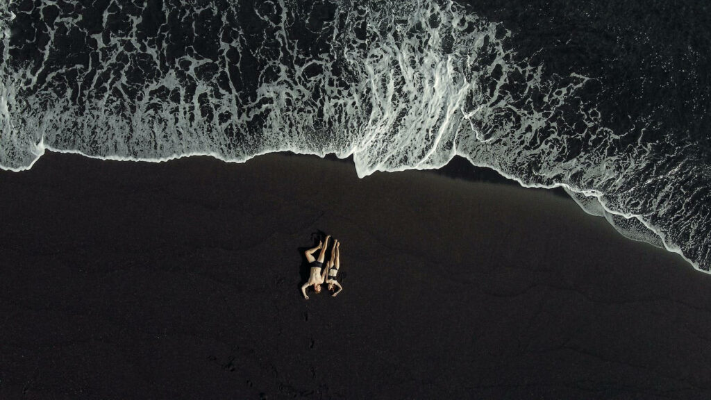 Enchanting Romance: Captivating Aerial Duo Resting on Black Sandy Beach Amidst Foamy White Waves - Full HD Love Background Wallpaper