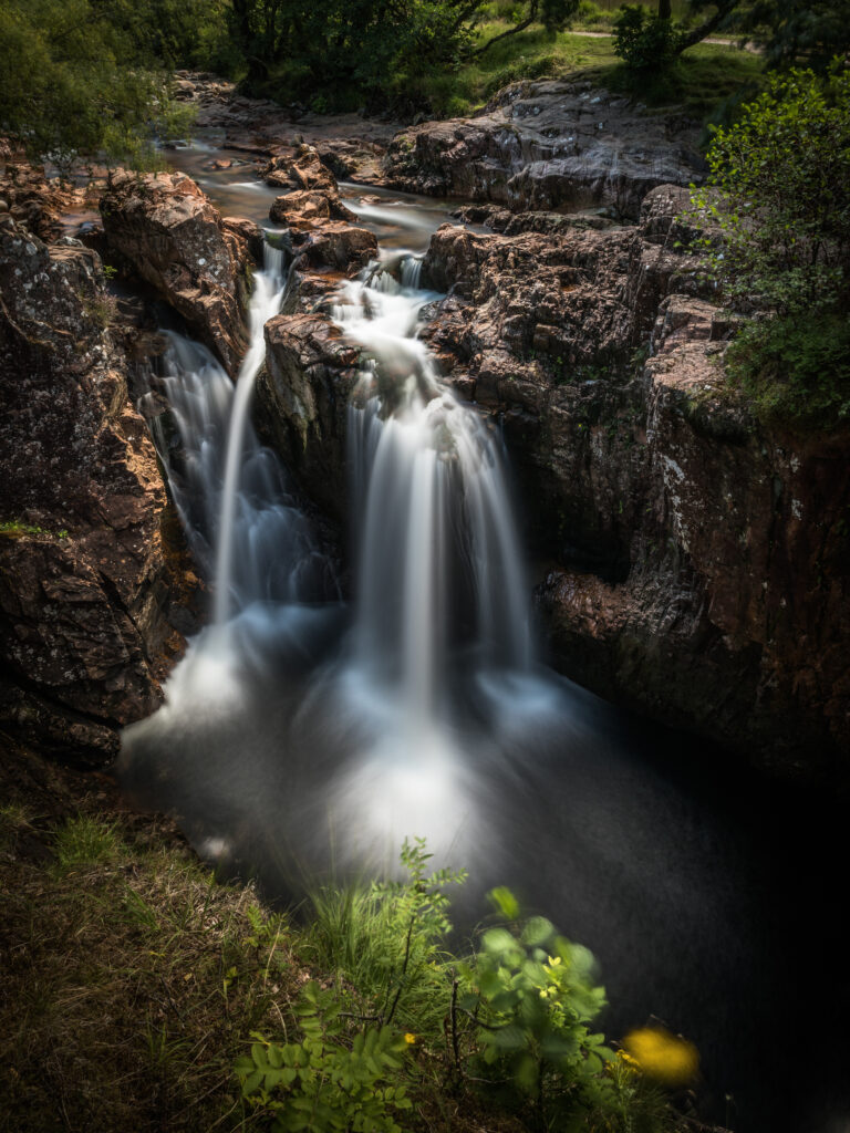 Waterfall cascading over rugged rocks surrounded by lush greenery peaceful natural landscape wallpaper