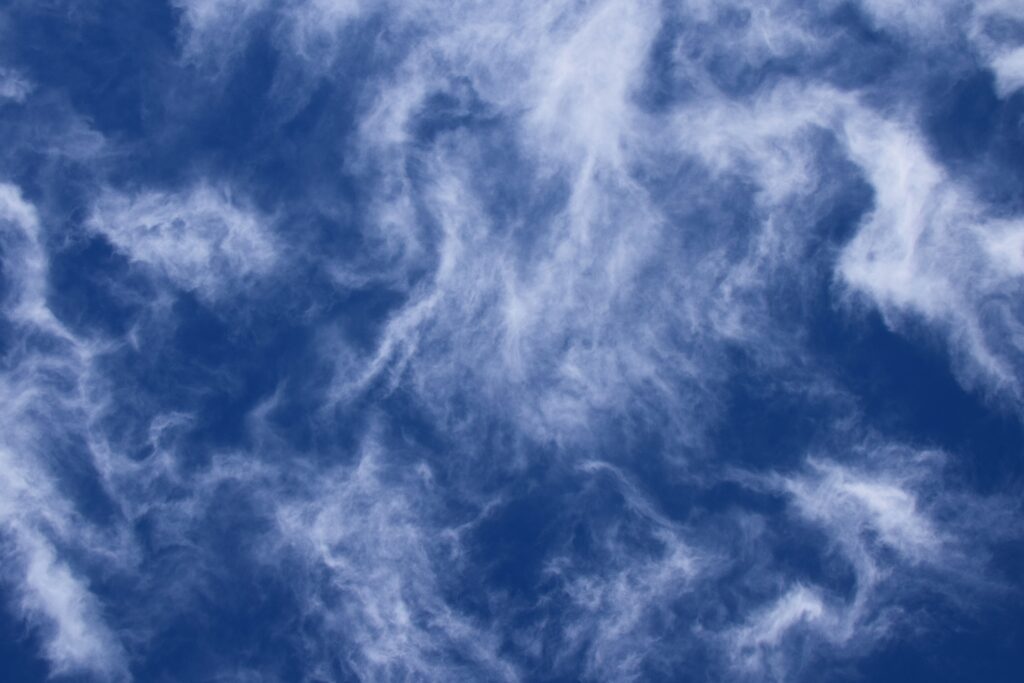 Wispy porous clouds drifting over a deep blue sky creating a serene airy wallpaper background
