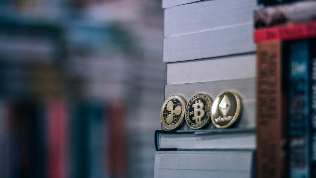 Ethereum Bitcoin and Ripple coins on stacked library books blending crypto and knowledge theme Wallpaper