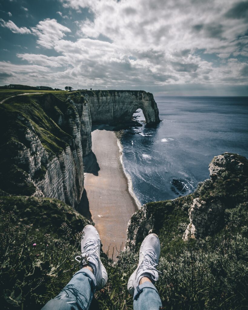 View from Etretat cliffs with sneakers foreground overlooking white chalk cliffs sea and sky Wallpaper